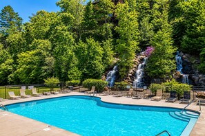 Una piscina amb diverses cascades, envoltada d'arbres verdosos i un cel serè.