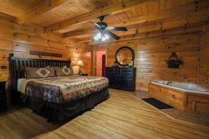A log cabin bedroom with a bed, dresser, vanity, and a bathtub. - A Time to Remember -Private Hot Tub • Game Room • Resort Pools (Sevierville)