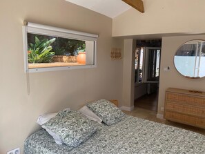Ein Schlafzimmer mit einem Bett, einem Fenster mit Pflanzen, einem Schminktisch und einem Spiegel.