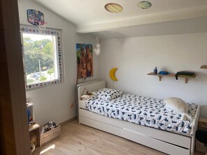 A child's bedroom with a bed, a crib, a window with a view, a wall with sports stickers, and a shelf with books. - Cozy 3BR Apt w/ AC Cassis (Cassis)