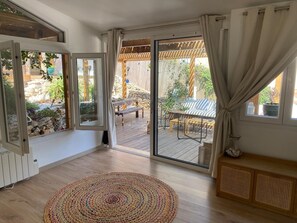 A room with a wooden floor, a large sliding glass door leading to an outdoor patio, a round woven rug, and a wooden bench. - Cozy 3BR Apt w/ AC Cassis (Cassis)
