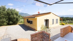 A small yellow building with a tiled roof, a door, and windows with shutters, surrounded by gravel and greenery. - Gaetano Spadaro Estate, La Rosa Room (Capannori)