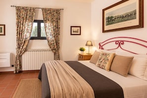 Une chambre à coucher avec un lit, une fenêtre avec des rideaux, une table de chevet avec une lampe et un tableau encadré au mur.