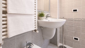 A bathroom with a white sink, a towel rack with folded towels, a potted plant, and a mirror. - Gaetano Spadaro Estate, La Rosa Room (Capannori)