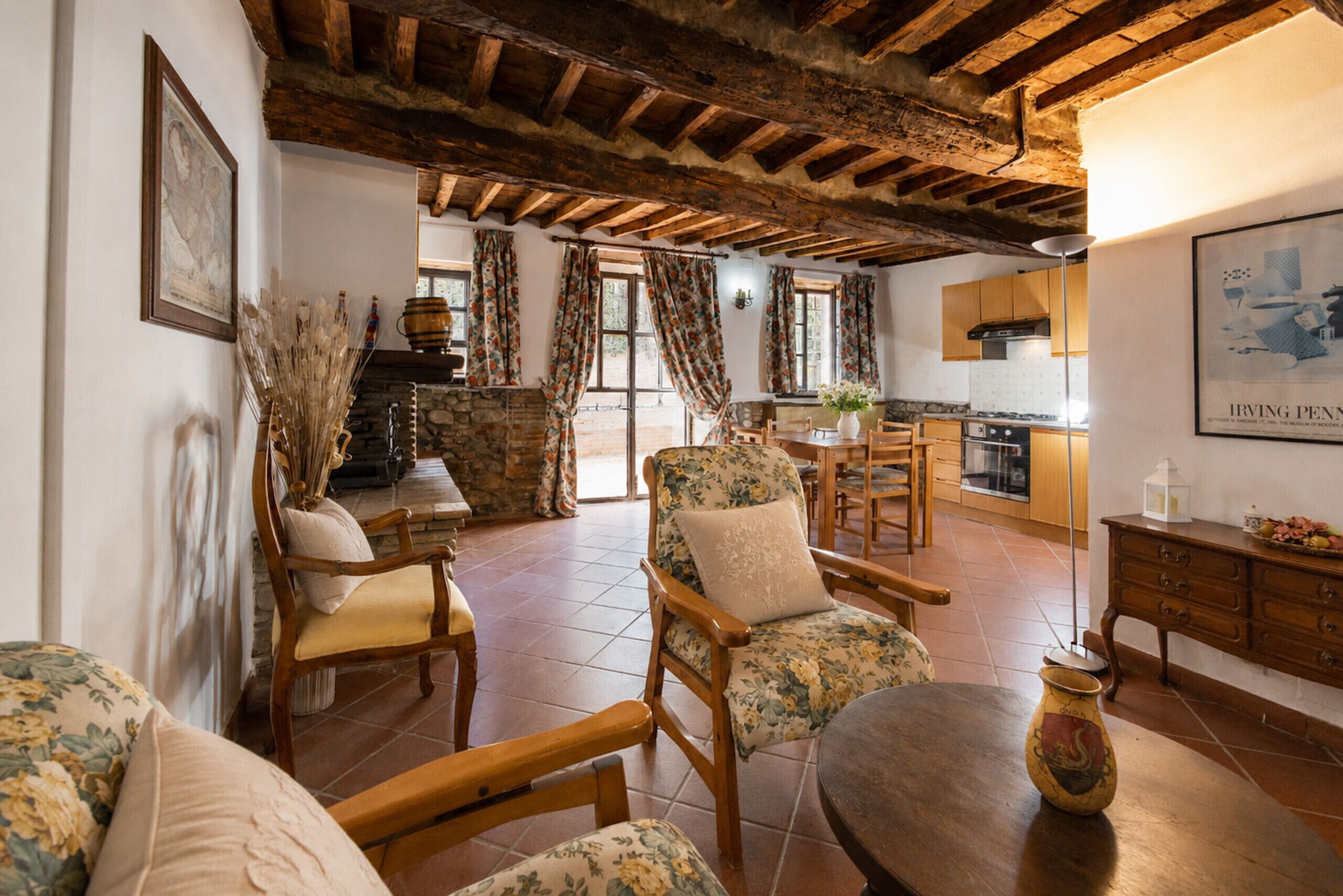 A rustic interior with exposed wooden beams, a stone fireplace, and a kitchen with wooden cabinets.