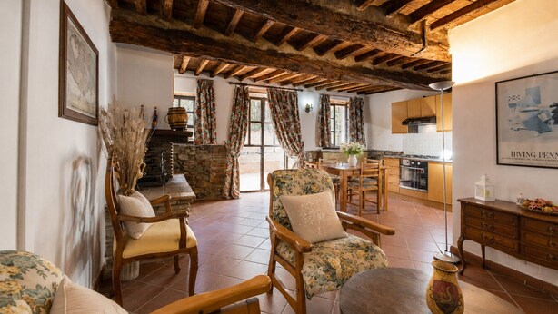 A rustic interior with exposed wooden beams, a stone fireplace, and a kitchen with wooden cabinets. - Gaetano Spadaro Estate, Leccino Apartment (Capannori)