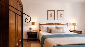 A neatly arranged bedroom with a wooden wardrobe, a bed with a green bedspread, two bedside lamps, and two framed botanical prints on the wall. - Gaetano Spadaro Estate, Leccino Apartment (Capannori)