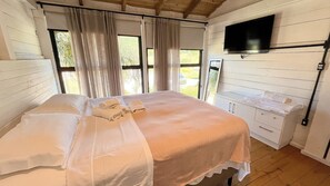 A bedroom with a bed, a TV mounted on the wall, and a window with curtains.