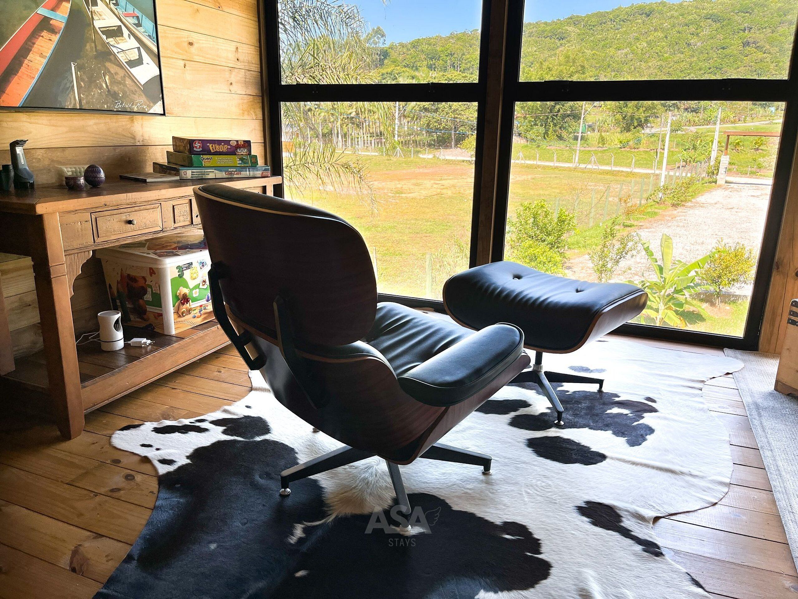 Una habitación con un ventanal grande, un escritorio de madera, una silla de cuero negro y un tapiz de piel de vaca.