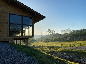 A wooden building with large windows and a view of a grassy field and trees.