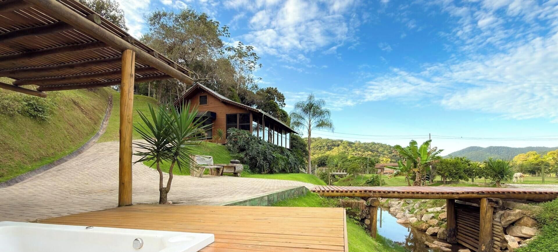 A wooden deck with a hot tub, a stone bridge, and a house with a sloped roof.