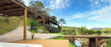 Eine Holzterrasse mit Whirlpool, einer Stegbrücke und einem Haus mit Schrägdach.