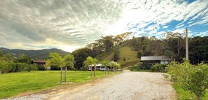 A rural road leading to a house surrounded by greenery and hills.
