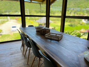 A wooden table with woven baskets and chairs in a room with large windows overlooking a green landscape.