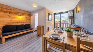 Ein gemütliches Zimmer mit einer Holz-Couch, einem Esstisch gedeckt mit Tellern und Gläsern und Blick auf Berge durch ein Fenster.