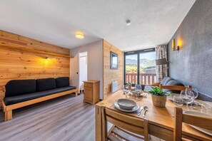 A cozy room with a wooden sofa, a dining table set with plates and glasses, and a view of mountains through a window. - Residence Altineige, Ski In-Out with WiFi in Val Thorens, “V8” by Versant Collection (Val Thorens)