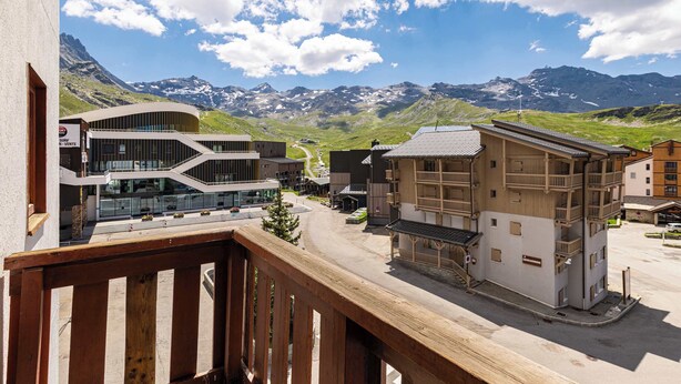 Ein modernes Gebäude mit Glasfassade und Holzbalkon mit Blick auf eine gebirgige Landschaft.