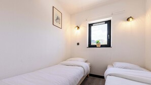 Ein kleines, sauberes Zimmer mit zwei Einzelbetten, einem Fenster mit Ausblick und einer Wandleuchte.
