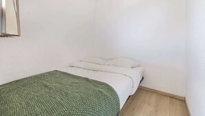 Ein kleiner Raum mit weißen Wänden, einem Einzelbett und einer grünen Decke.