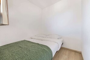 Ein kleiner Raum mit weißen Wänden, einem Einzelbett und einer grünen Decke.