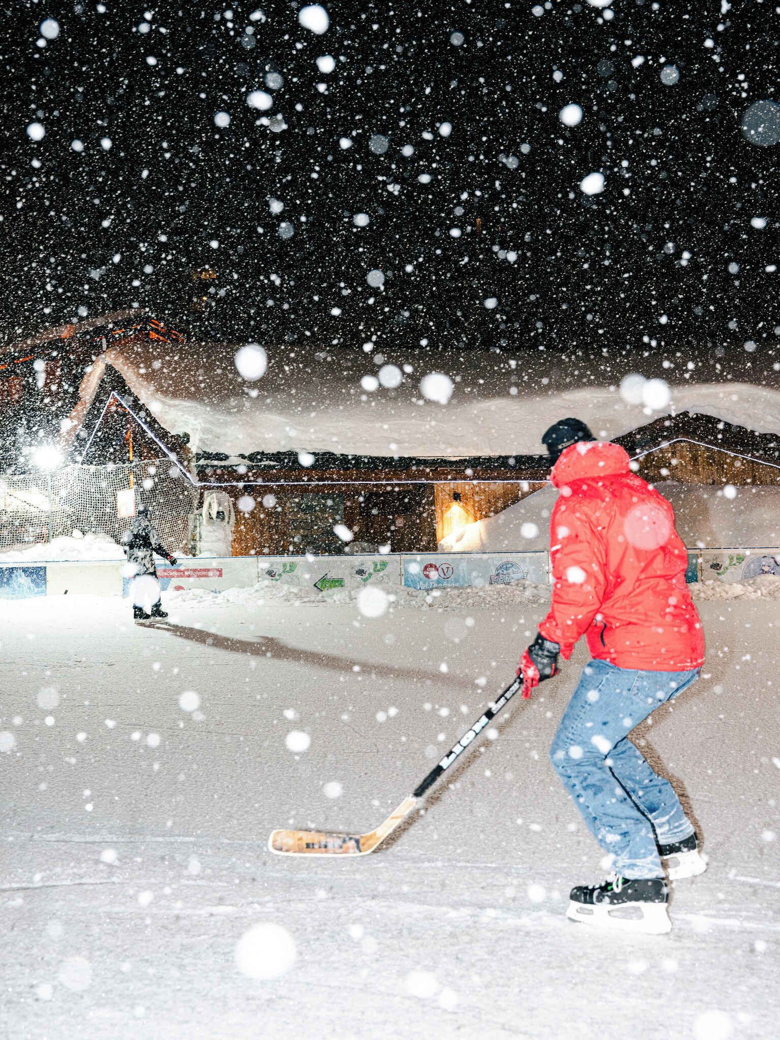 Eine Person ist auf einem verschneiten Hang beim Skifahren, im Hintergrund ist ein Gebäude zu sehen.