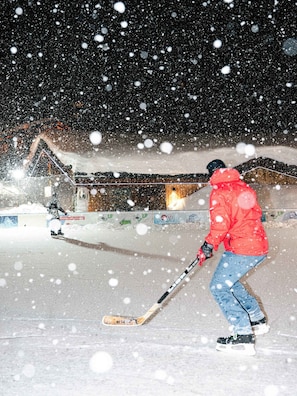 Eine Person ist auf einem verschneiten Hang beim Skifahren, im Hintergrund ist ein Gebäude zu sehen.