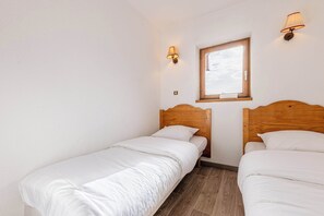 A small, clean room with two single beds, a window, and wall-mounted lights. - Residence Altineige, Ski In-Out with WiFi in Val Thorens, “V9” by Versant Collection (Val Thorens)