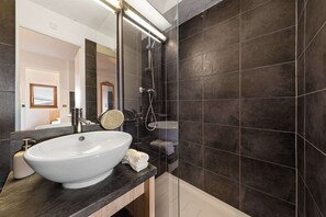 A modern bathroom with a white sink, dark tiled walls, and a glass shower enclosure. - Residence Altineige, Ski In-Out with WiFi in Val Thorens, “V9” by Versant Collection (Val Thorens)