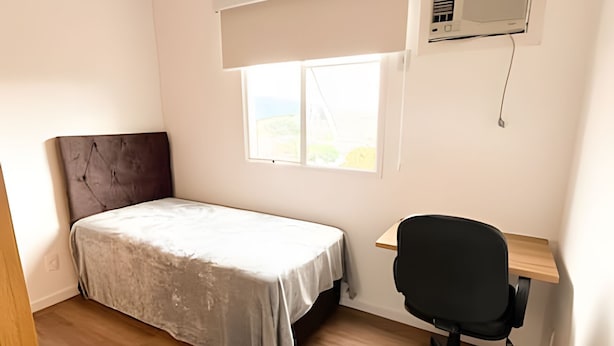 Een slaapkamer met een bed, een bureau en een stoel. Er is een raam met uitzicht op het omliggende landschap.