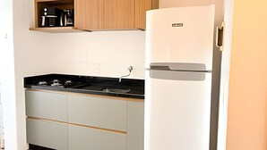 Een kleine keuken met een zwart fornuis, witte kasten en een witte koelkast.