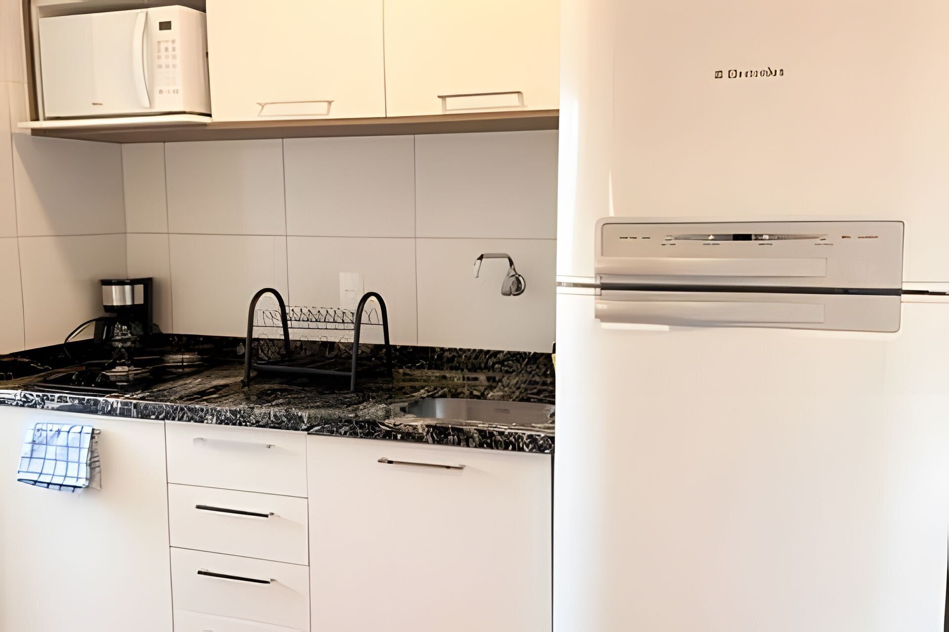 Una cocina con armarios blancos, un refrigerador de acero inoxidable, una cafetera y un lavamanos.