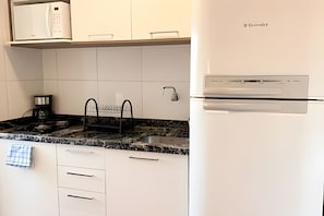 A kitchen with white cabinets, a stainless steel refrigerator, a coffee machine, and a sink.