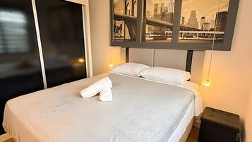 Habitación de hotel con una cama, una mesita de noche y una obra de arte en la pared que muestra un paisaje urbano.