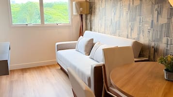 Een moderne woonkamer met een bank, een ronde houten tafel en uitzicht op groen door het raam.