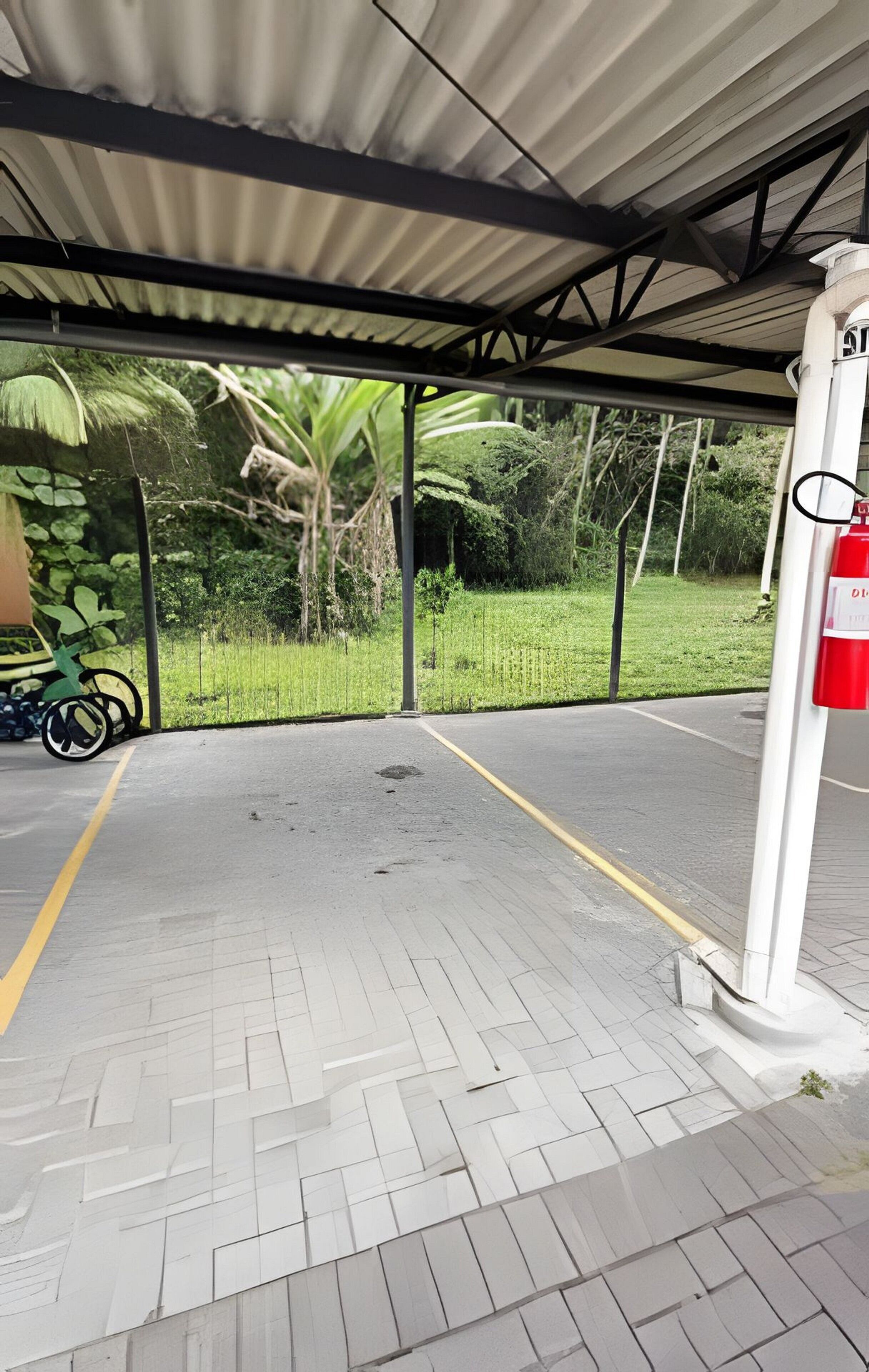 Een overdekte parkeerplaats met verhard oppervlak, een brandblusser en een motorfiets aan de zijkant.