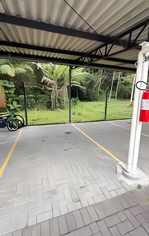 Un área de estacionamiento techada con superficie pavimentada, un extintor y una motocicleta estacionada a un lado.