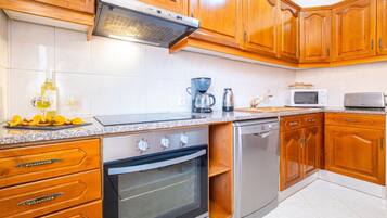 Una cocina con armarios de madera, horno empotrado, lavavajillas, cafetera y microondas.