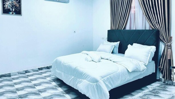 A neatly made bed with white bedding in a room with a marble-patterned floor. - Legon hills hotel and suits (Adenta)