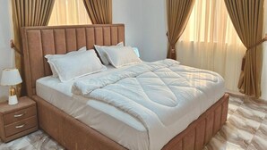 A bedroom with a bed, curtains, a bedside table, and a lamp. - Legon hills hotel and suits (Adenta)