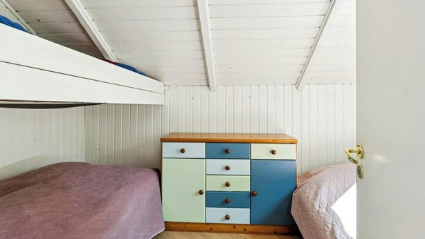 A small, single-bed room with a bunk bed above, a wooden dresser with multiple drawers, and a door with a golden handle. - Holiday home with garden and wildlife in Gjern (Truust)