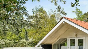 A modern house with a deck, two lounge chairs, and a glass door leading to a covered patio. - Holiday home with garden and wildlife in Gjern (Truust)