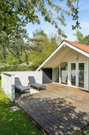 Ein modernes Haus mit einer Terrasse, zwei Liegestühlen und einer Glastür zu einer überdachten Veranda.