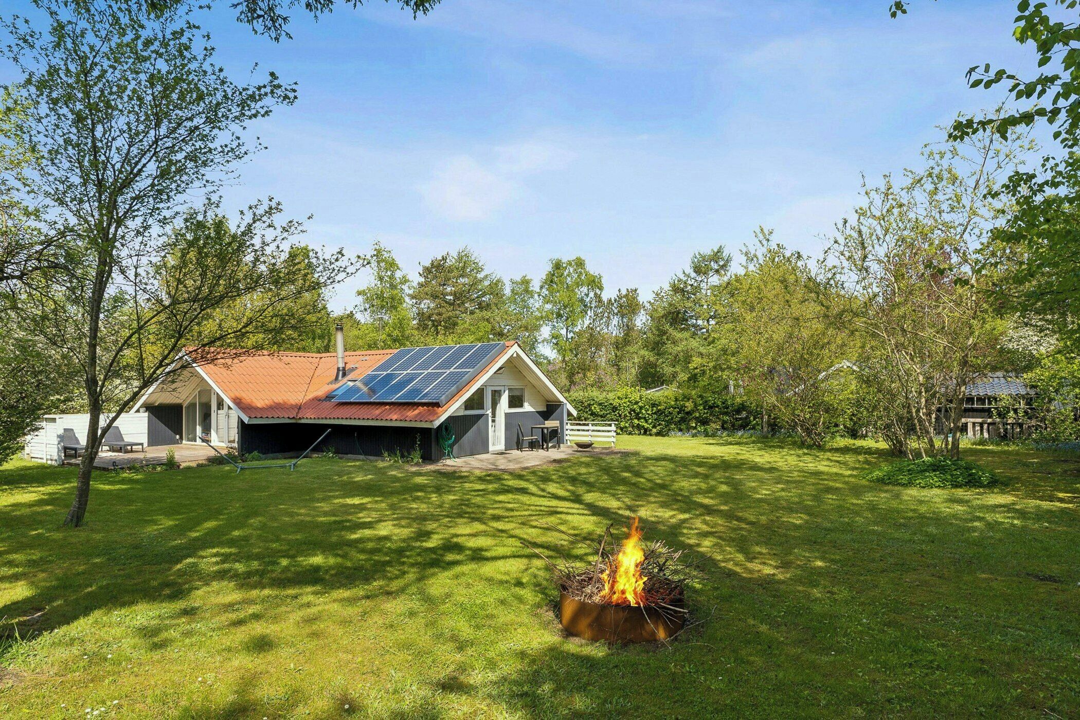 Une maison avec un toit en pente, des panneaux solaires et un foyer extérieur dans le jardin.