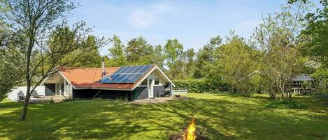 Een huis met schuin dak, zonnepanelen en een vuurkuil in de tuin.
