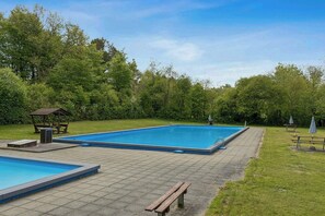 Ein rechteckiger Swimmingpool mit einer umlaufenden Holzterrasse, Bänken und einem Pavillon.