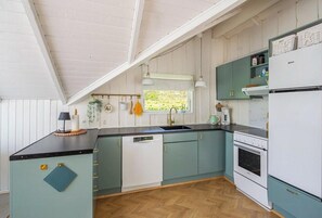 Eine Küche mit Holzdielen im Fischgrätmuster, weißen und türkisfarbenen Schränken, einem weißen Kühlschrank und einem Fenster mit Blick auf Grünflächen.