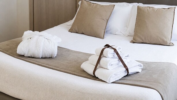 Una cama bien hecha con sábanas blancas, dos almohadas color beige y un cabecero marrón.