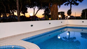 Una piscina de borde curvo, rodeada por un muro blanco y árboles.