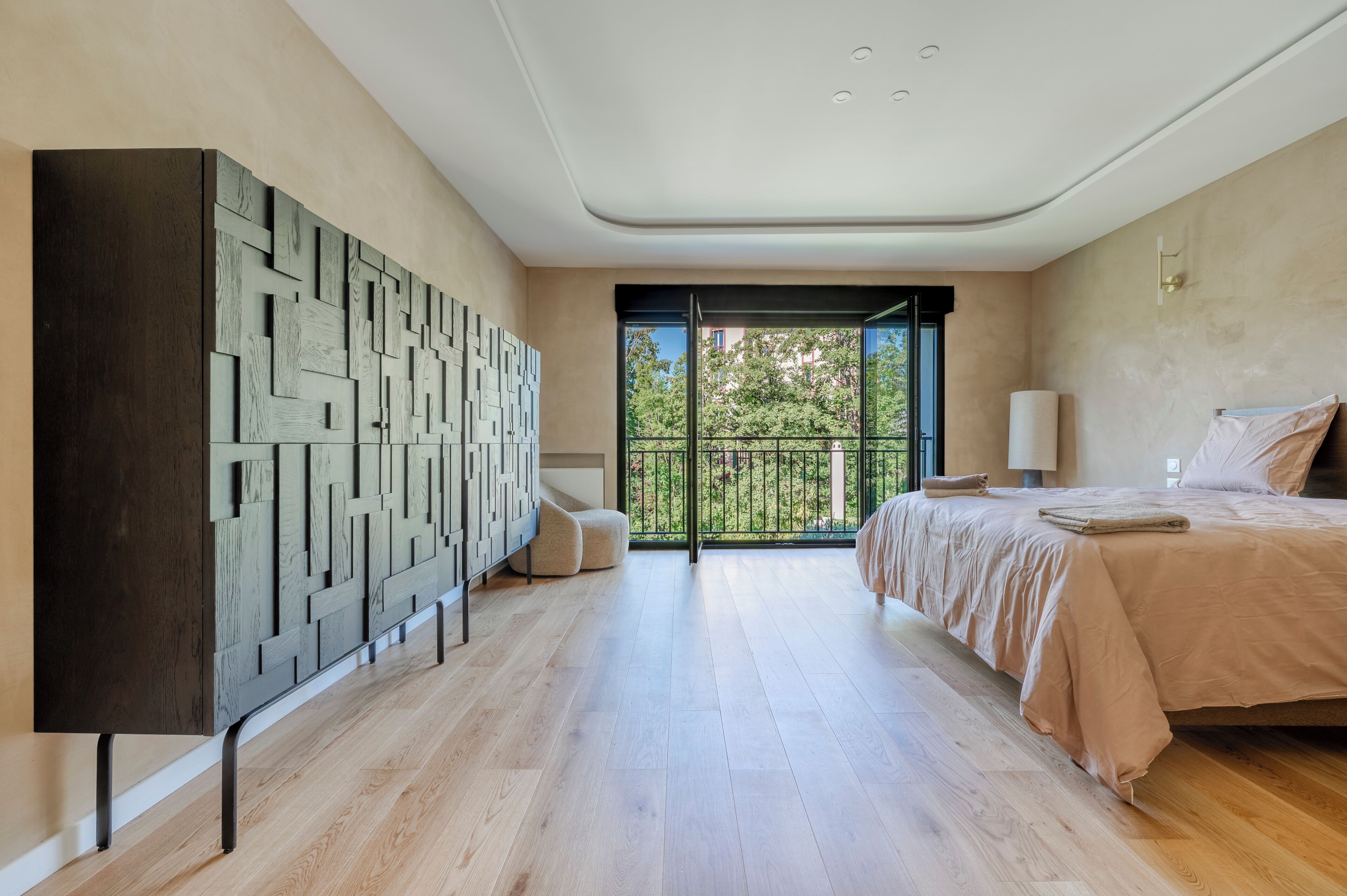 A bedroom with a large bed, a TV, and a balcony with a view of trees.