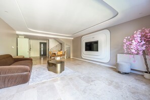 A modern living room with a brown sofa, a metallic coffee table, and a flat-screen TV mounted on the wall. - Exceptional Home • 4 Suites • Along the Marne River • Joinville (Joinville-le-Pont)